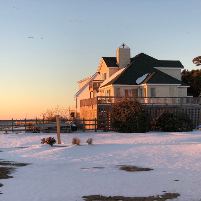 Charming beach house in Kill Devil Hills, NC, covered in snow during a serene sunset.